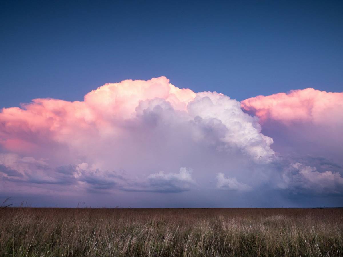 A towering storm cloud over open prairie at dusk